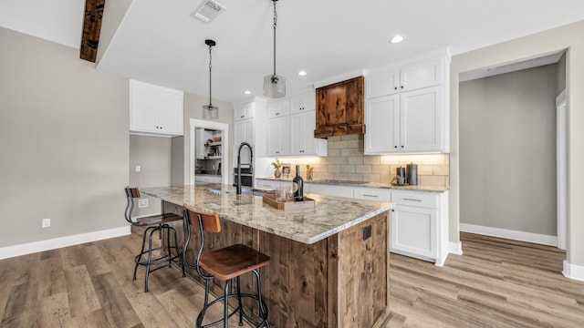 kitchen featuring light hardwood / wood-style flooring, white cabinetry, light stone counters, and a kitchen island with sink