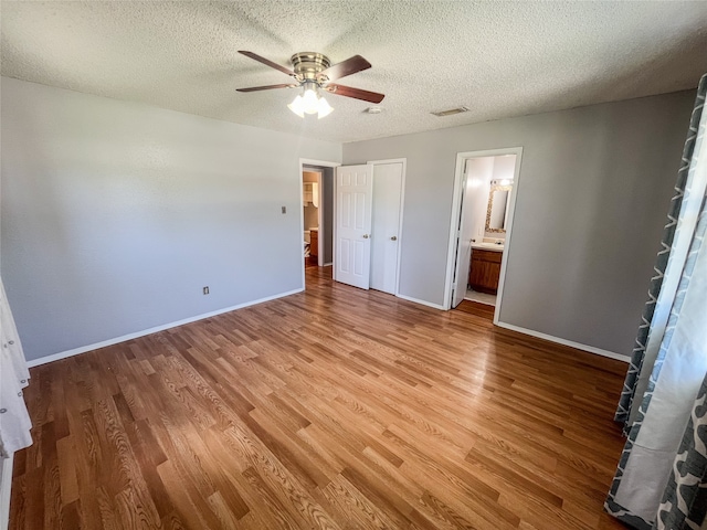 unfurnished bedroom with wood-type flooring, a textured ceiling, ensuite bath, and ceiling fan