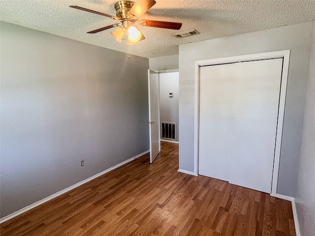 unfurnished bedroom featuring a closet, a textured ceiling, hardwood / wood-style flooring, and ceiling fan