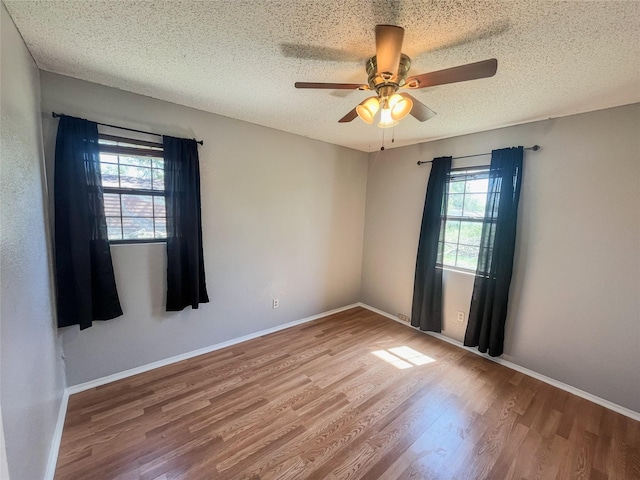 unfurnished room with a textured ceiling, wood finished floors, a ceiling fan, and baseboards