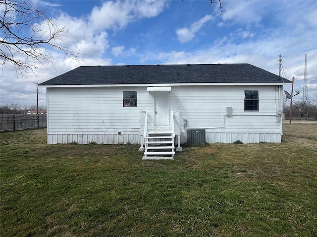 rear view of property with central air condition unit, fence, and a yard