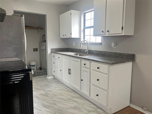 kitchen with marble finish floor, dark countertops, freestanding refrigerator, electric water heater, and white cabinetry