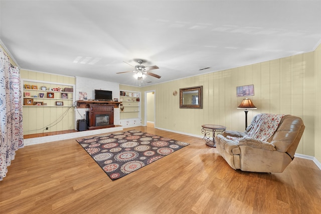 living room with ceiling fan, built in features, wooden walls, a fireplace, and light hardwood / wood-style floors