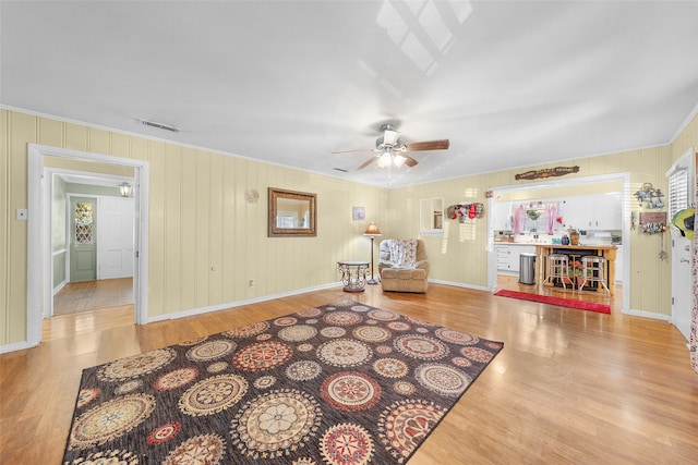 living area featuring ceiling fan, light wood-type flooring, and ornamental molding