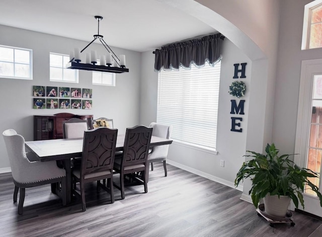 dining space with baseboards, wood finished floors, and arched walkways
