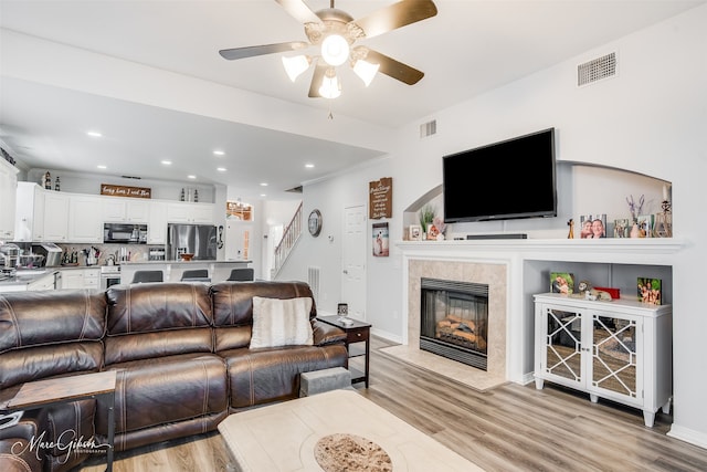 living room with ceiling fan, light wood-type flooring, a tiled fireplace, and crown molding