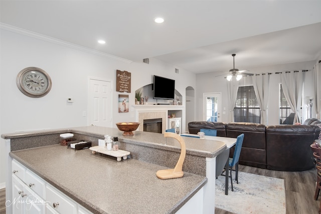 kitchen featuring white cabinets, a tile fireplace, crown molding, ceiling fan, and dark hardwood / wood-style floors