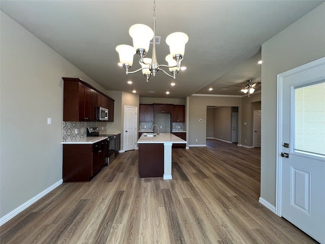 kitchen featuring backsplash, a center island with sink, ceiling fan with notable chandelier, dark hardwood / wood-style flooring, and stainless steel appliances