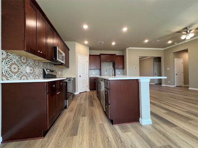 kitchen with sink, stainless steel appliances, decorative backsplash, a center island with sink, and light wood-type flooring