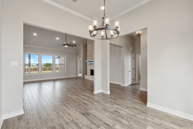 interior space with light wood-type flooring, lofted ceiling, a stone fireplace, ceiling fan with notable chandelier, and crown molding