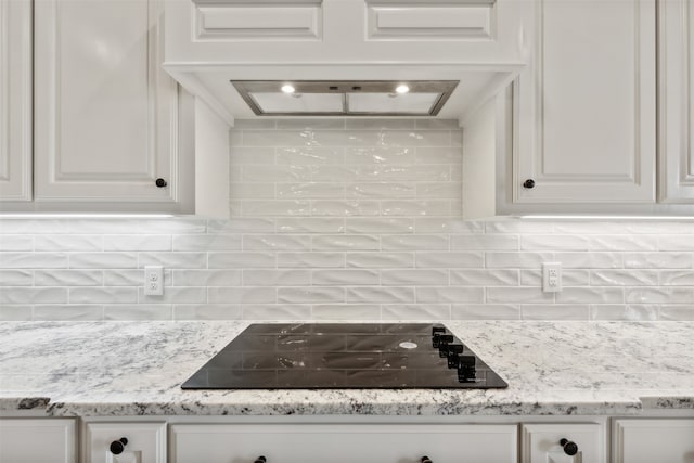 kitchen with black electric cooktop, white cabinets, light stone countertops, and tasteful backsplash