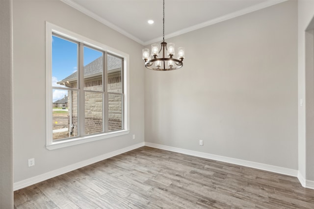 spare room with a notable chandelier, wood-type flooring, plenty of natural light, and ornamental molding