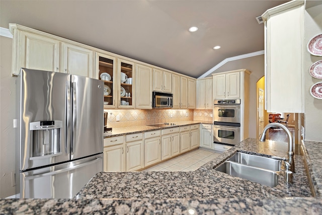 kitchen featuring sink, cream cabinetry, appliances with stainless steel finishes, dark stone countertops, and vaulted ceiling