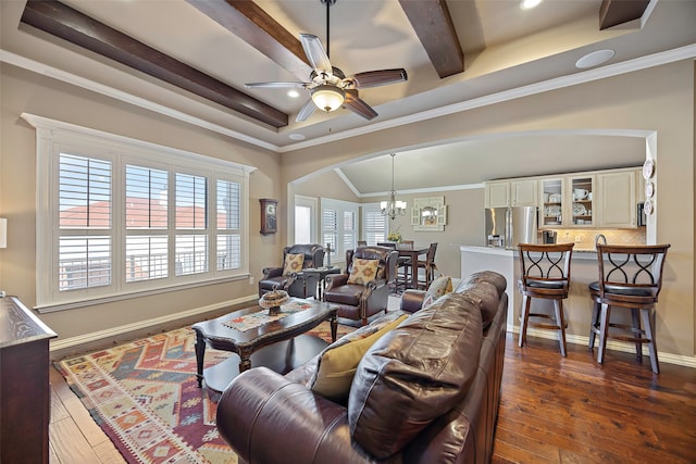 living room with beamed ceiling, a raised ceiling, ornamental molding, dark wood-type flooring, and ceiling fan with notable chandelier