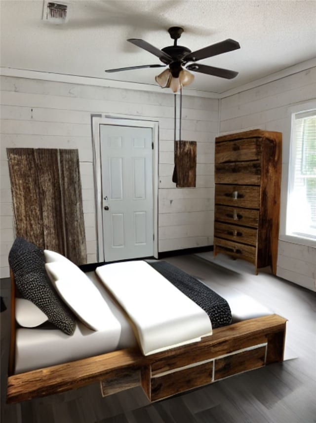 bedroom with a textured ceiling, wooden walls, ceiling fan, and hardwood / wood-style flooring