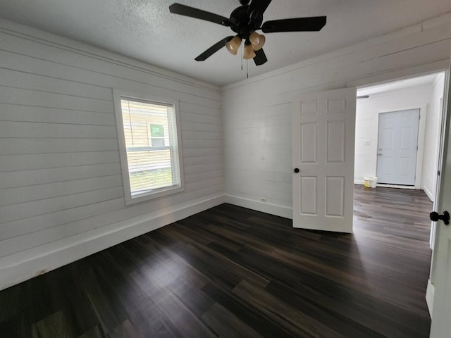 empty room featuring a textured ceiling, wood walls, ceiling fan, and dark wood-type flooring