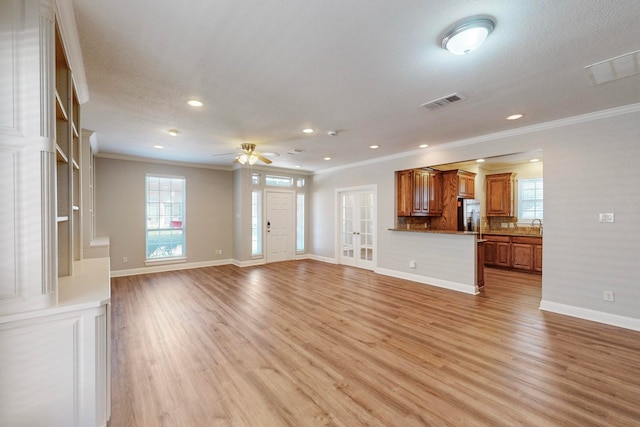 unfurnished living room with light wood-type flooring, a textured ceiling, sink, ornamental molding, and ceiling fan