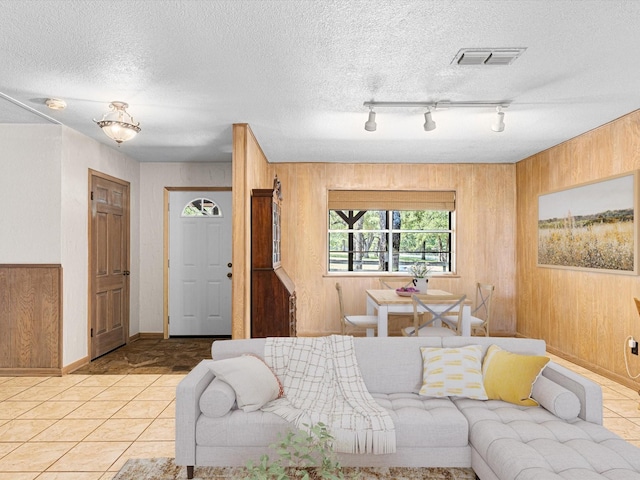 living room with a textured ceiling, track lighting, wood walls, and light tile patterned floors