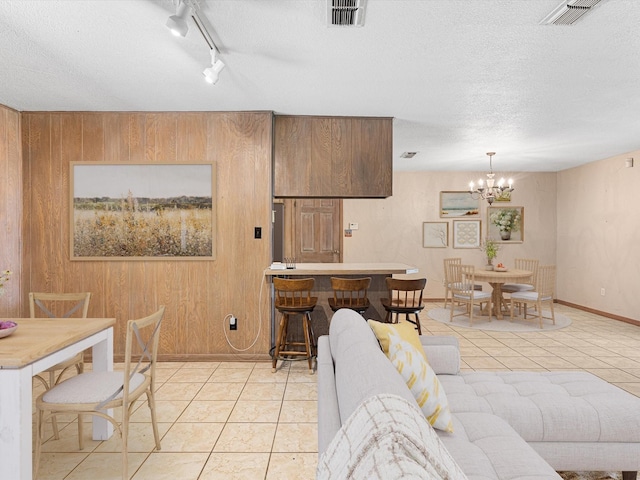 living room with a textured ceiling, light tile patterned floors, track lighting, wood walls, and a notable chandelier