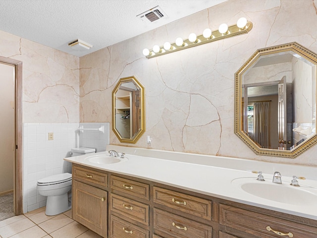 bathroom featuring toilet, a textured ceiling, tile patterned flooring, tile walls, and vanity