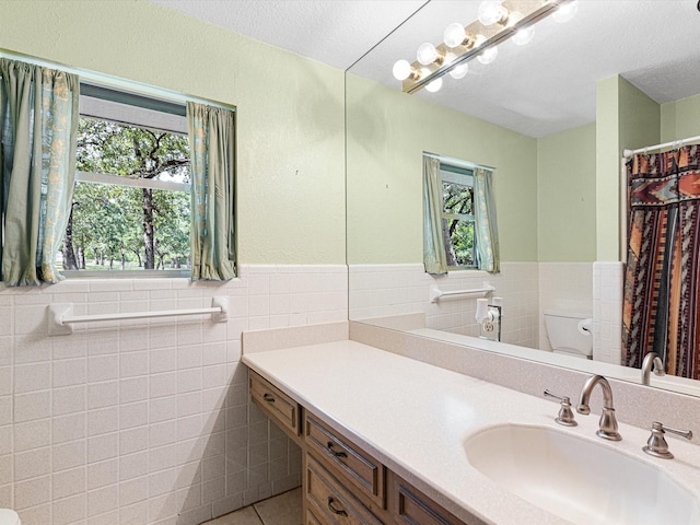 bathroom with toilet, tile patterned flooring, tile walls, and vanity