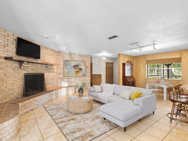 tiled living room with a fireplace, track lighting, wood walls, and a textured ceiling