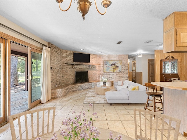 living room featuring a textured ceiling, a brick fireplace, an inviting chandelier, and light tile patterned floors