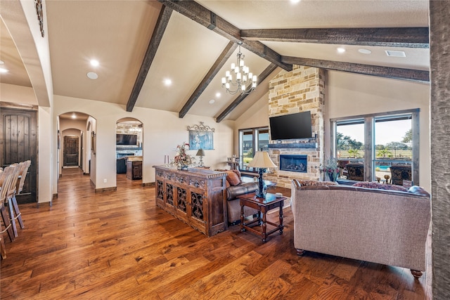 living room with beam ceiling, wood-type flooring, a stone fireplace, a chandelier, and high vaulted ceiling