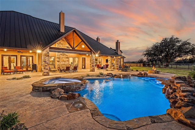 pool at dusk with an in ground hot tub, pool water feature, and a patio area