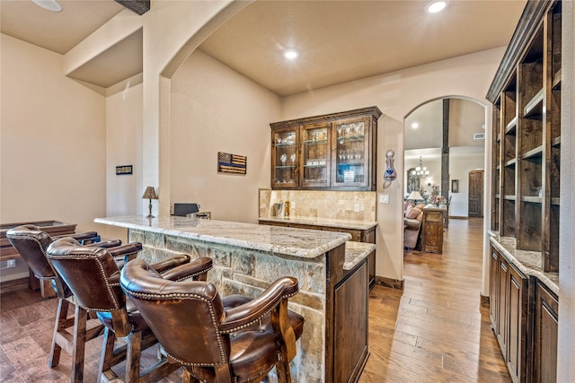 bar featuring backsplash, light stone counters, dark brown cabinetry, and dark hardwood / wood-style flooring