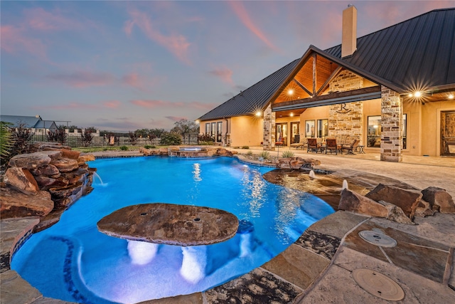 pool at dusk featuring an in ground hot tub, a patio, and pool water feature