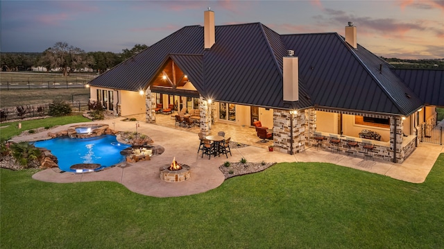 back house at dusk with a lawn, a pool with hot tub, and a patio area