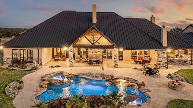 pool at dusk with a patio, an in ground hot tub, and pool water feature