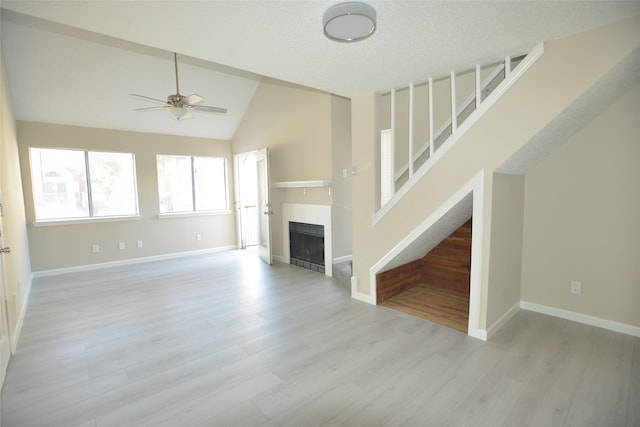 unfurnished living room featuring ceiling fan, light wood-type flooring, a tiled fireplace, and lofted ceiling