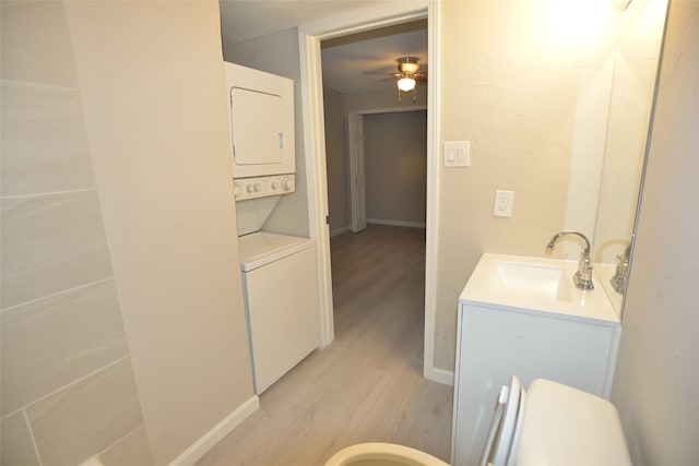 bathroom with ceiling fan, vanity, toilet, stacked washer / dryer, and hardwood / wood-style floors