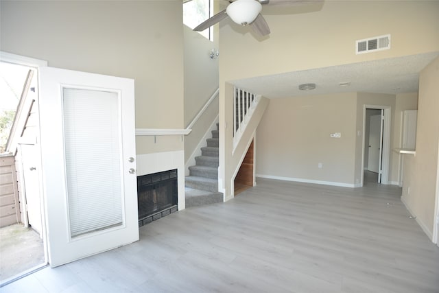 unfurnished living room with light hardwood / wood-style floors, ceiling fan, a tile fireplace, and a textured ceiling