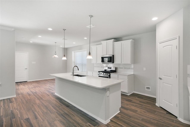 kitchen with stainless steel appliances, a center island with sink, sink, decorative light fixtures, and white cabinets