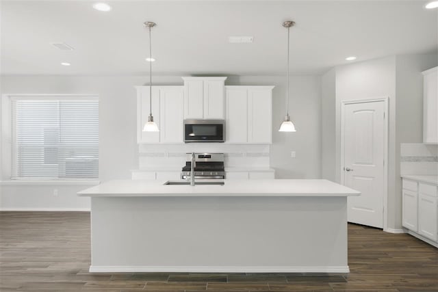 kitchen with a center island with sink, white cabinets, dark hardwood / wood-style floors, pendant lighting, and appliances with stainless steel finishes