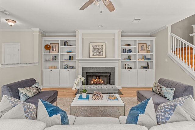 living room featuring ceiling fan, ornamental molding, a fireplace, and light hardwood / wood-style floors