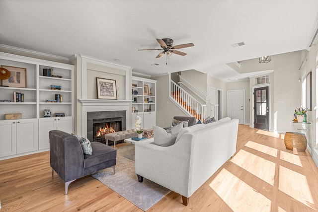 living room featuring light hardwood / wood-style flooring, ornamental molding, ceiling fan, and a fireplace