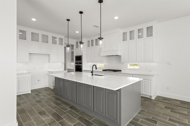 kitchen featuring decorative light fixtures, sink, white cabinets, stainless steel appliances, and a center island with sink