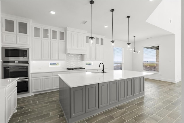 kitchen featuring built in microwave, sink, an island with sink, and white cabinets