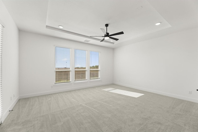 spare room featuring a raised ceiling, light colored carpet, and ceiling fan