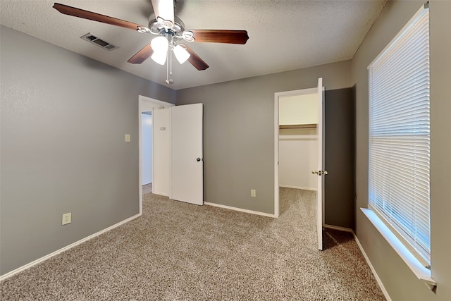 unfurnished bedroom with a textured ceiling, a spacious closet, ceiling fan, and light colored carpet