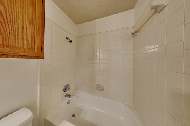 bathroom with a textured ceiling, tiled shower / bath combo, and toilet