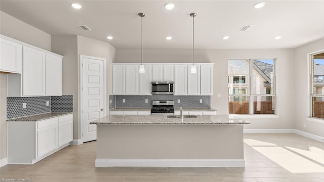 kitchen with a center island with sink, pendant lighting, stainless steel appliances, and white cabinets