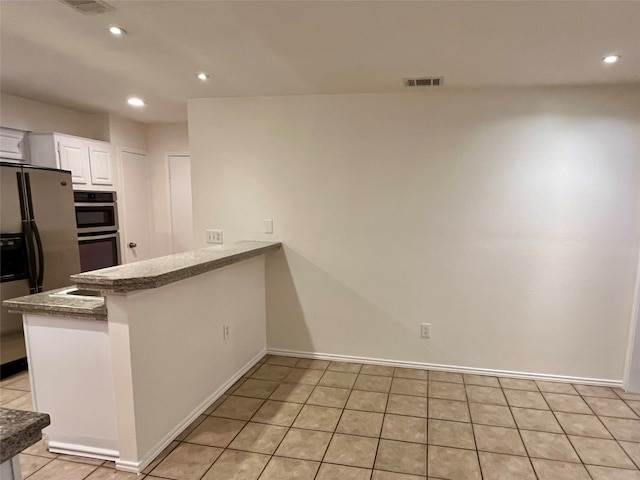 kitchen with appliances with stainless steel finishes, kitchen peninsula, light tile patterned flooring, and white cabinets