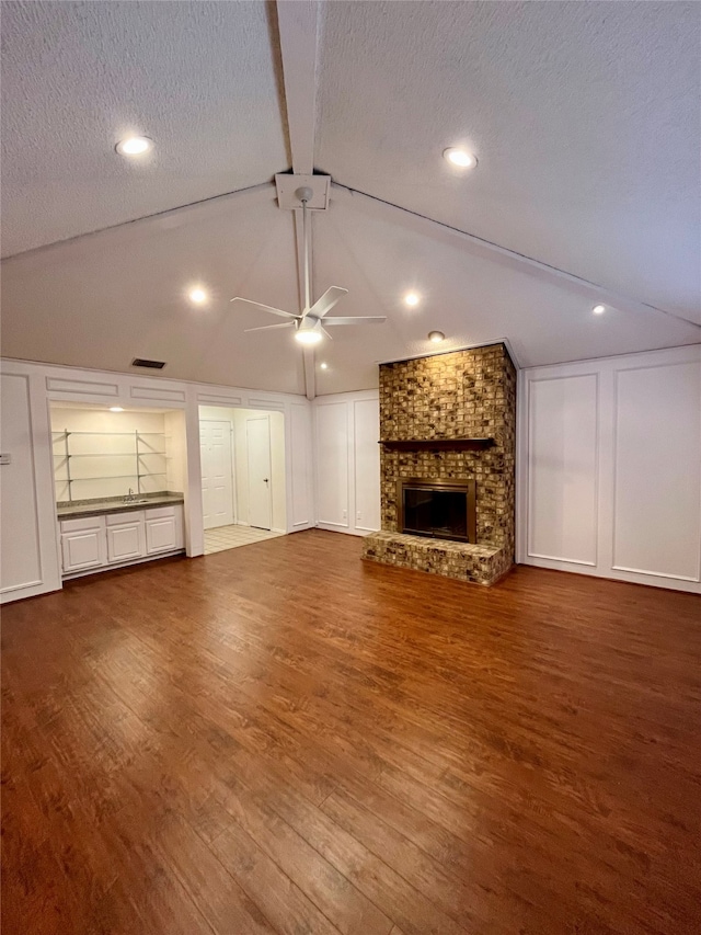 unfurnished living room with a brick fireplace, a textured ceiling, ceiling fan, hardwood / wood-style flooring, and vaulted ceiling with beams