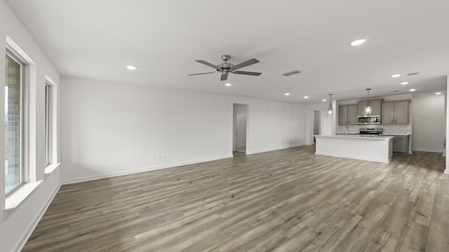 unfurnished living room featuring hardwood / wood-style floors, sink, and ceiling fan