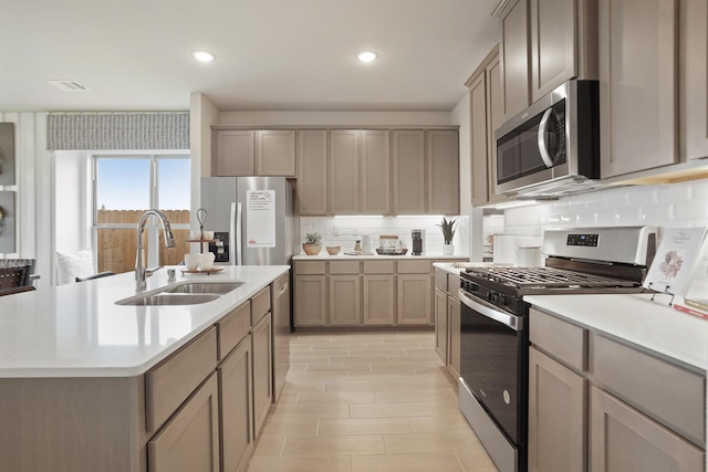 kitchen featuring decorative backsplash, appliances with stainless steel finishes, an island with sink, and sink